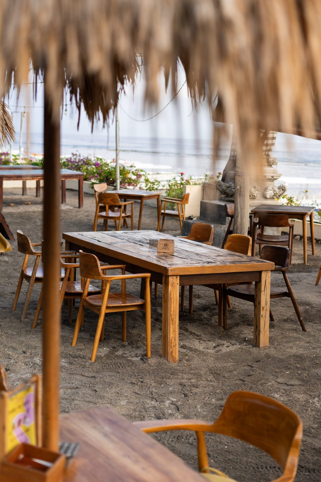 Long communal teak table on the sand with bougainvillea and the sea behind
